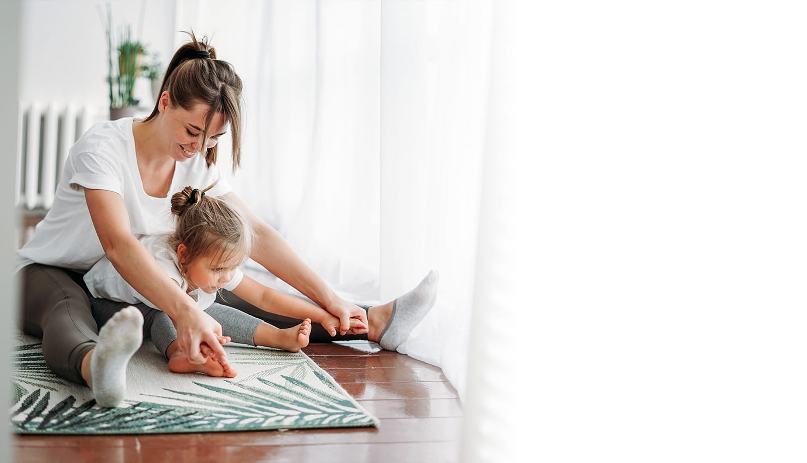 Mujer y niña practicando yoga en casa sobre una alfombra